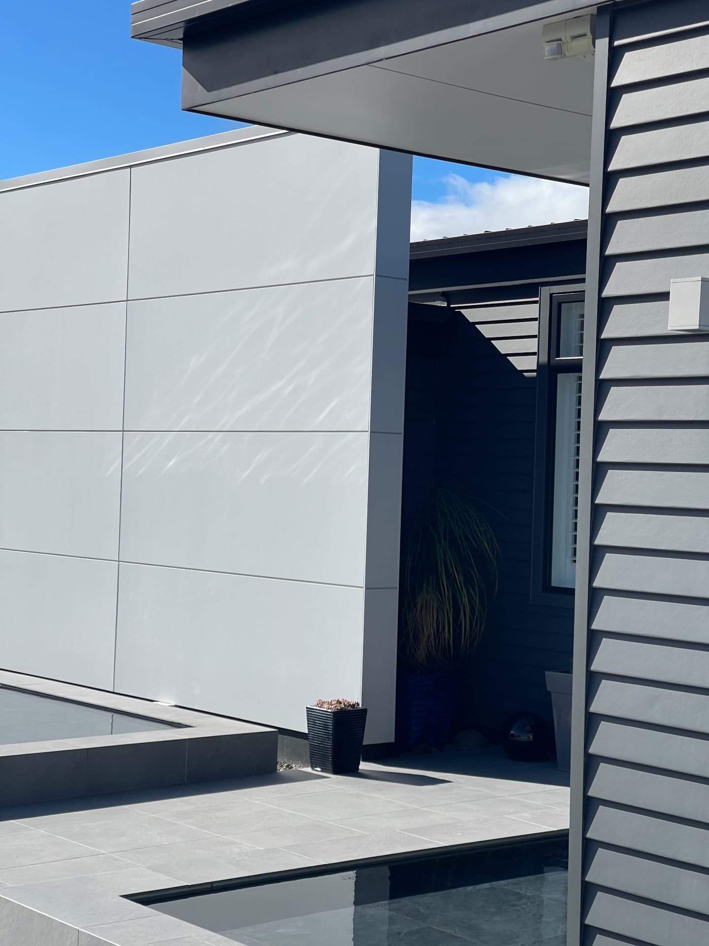 Pale panelled wall meeting dark weatherboard around a still courtyard pool